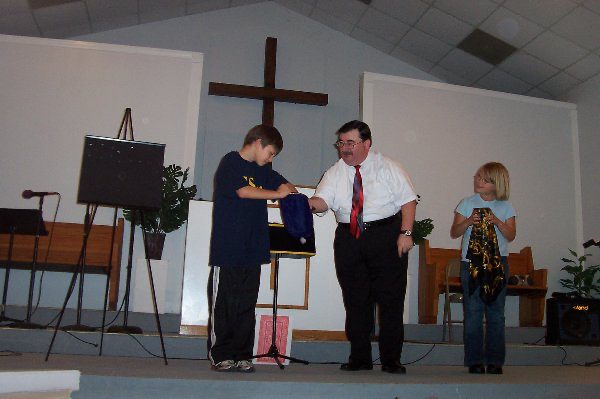 Ken Sibley presenting a Gospel illusion on stage with two young helpers